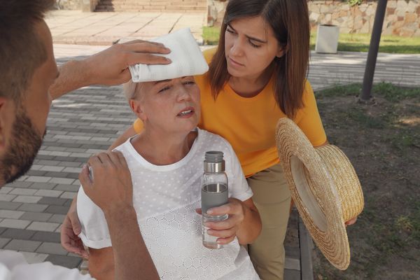 A man and woman help an elderly woman as she's having a heat stroke. The risk of heat stroke in the elderly