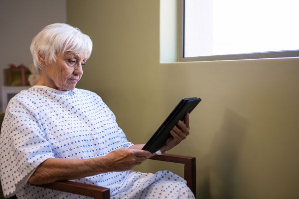 Elderly woman in a nursing home gown on a tablet. Illinois nursing home ratings over the years.