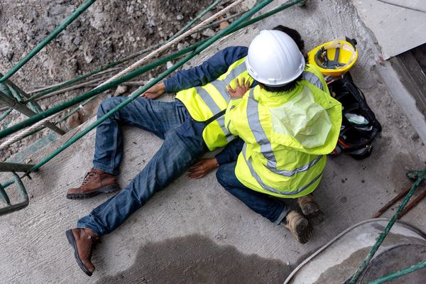 a construction worker is injured on the ground while another construction worker helps him. common accidents in construction