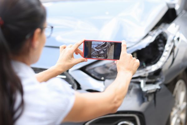 Woman taking pictures of her car after a car accident. Who do you sue in a car accident case?