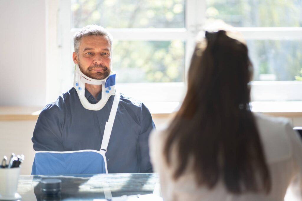 Joliet personal injury attorney - Injured man in an arm sling and neck brace sitting at a desk in front of an injury attorney 